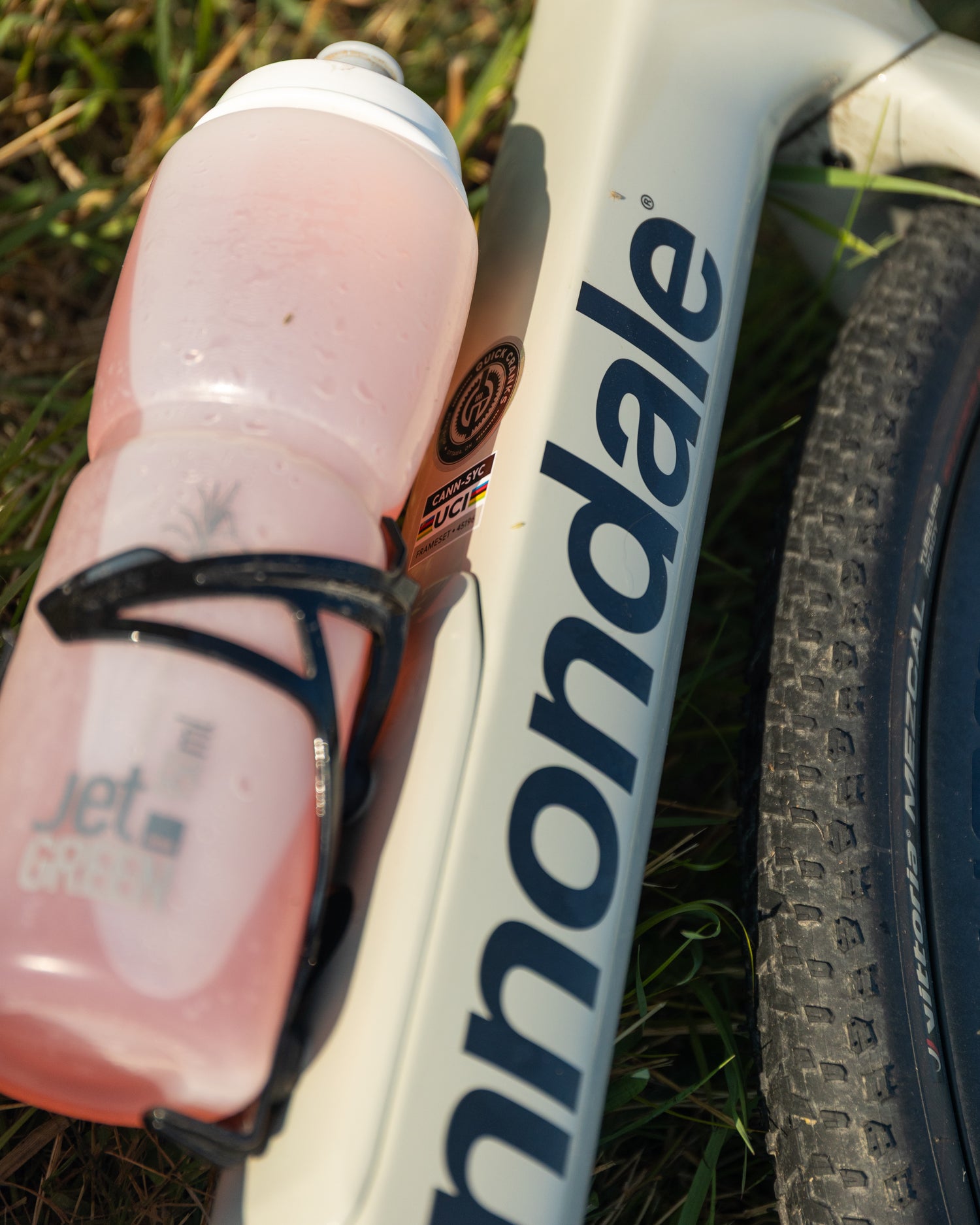 Bicycle water bottle holder with a bottle attached, featuring cannondale branding on a grassy background.